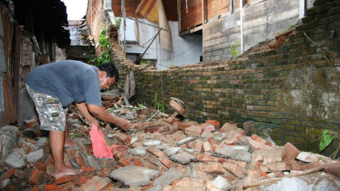 À Padang, un homme ramasse les débris d'un mur de briques qui s'est effondré.
