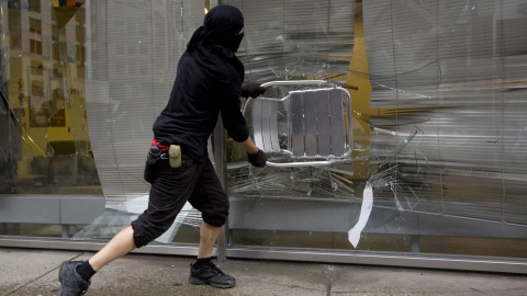 Un manifestant utilise une chaise pour fracasser une vitrine.