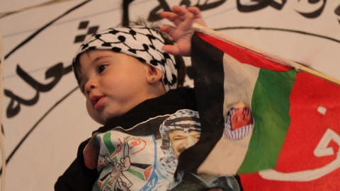 Une fillette palestinienne, v�tue d'un chandail � l'effigie de Yasser Arafat, assiste aux c�r�monies en agitant un fanion palestinien.
