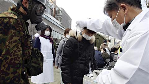 Un médecin vérifie le taux de radiation d'une femme sous le regard d'un militaire, dans la préfecture de Fukushima.