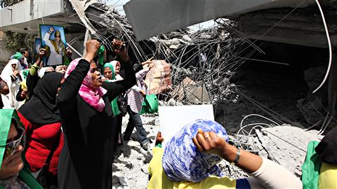 Des partisans de Mouammar Kadhafi protestent devant une maison de Tripoli détruite la veille par les forces de l'OTAN, selon le régime