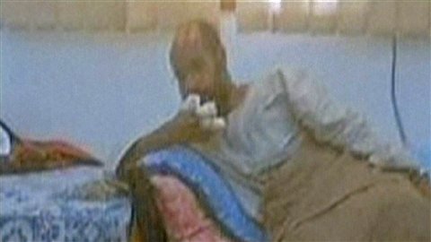 Photo de la chaîne de télévision Free Libya montrant Saïf al Islam, main bandée, les jambes sous une couverture, assis sur un canapé, après son arrestation. 
