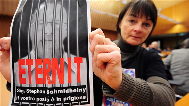 Au tribunal de Turin, une femme brandit une affiche sur laquelle est écrit : Stephan Schmidheiny ta place est en prison.