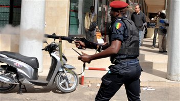 Policer sénégalis en train de tirer une grenafe lacrymogène.