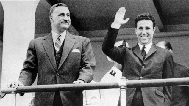 الرئيس المصري جمال عبد الناصر خلال زيارة له إلى الجزائر في 3 أيار (مايو) 1963 يقف إلى جانب نظيره الجزائري أحمد بن بلا الذي يرفع يده محيياً الجموع.