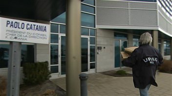 Un enquêteur de l'UPAC transporte des boîtes de carton sur les lieux de la perquisition.