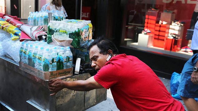 Dans la canicule à New York, un vendeur itinérant pousse son chariot rempli de bouteilles d'eau.