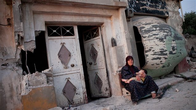 Une femme tient son petit fils dans ses bras devant une maison en ruine du village de Treimsa, en Syrie.