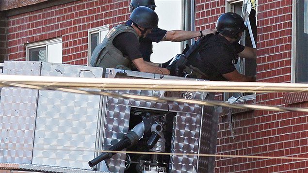 Des policiers inspectent l'appartement du suspect depuis la nacelle d'un camion de pompier.