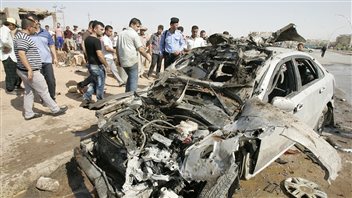 Policiers et piétons observent la carcasse d'une voiture piégée à Kirkouk, le 23 juillet 2012