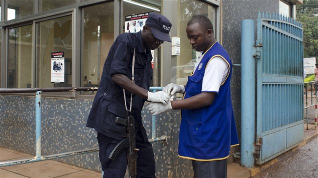 Un policier aide un travailleur à mettre ses gants à l'entrée de l'Hôpital Mulago, à Kampala.