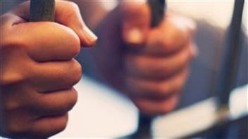 Les mains d'un détenu sur les barreaux d'une cellule