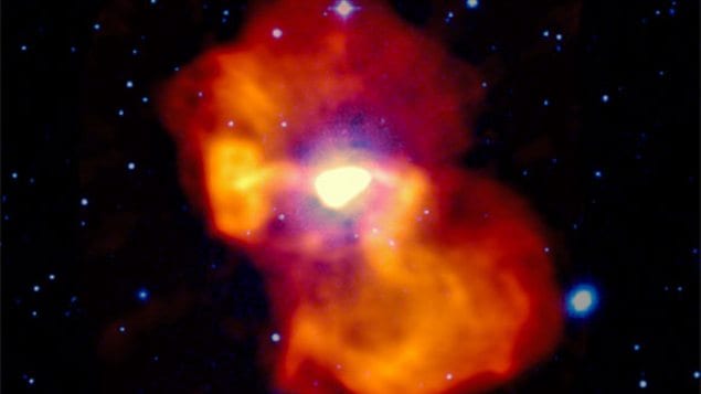 L'Image en fausses couleurs de la galaxie M 87. La lumière visible apparaît en blanc et bleu. L'émission radio est codée en jaune-orangé. Au centre, l'émission radio très intense provient du jets de particules propulsé par le trou noir.