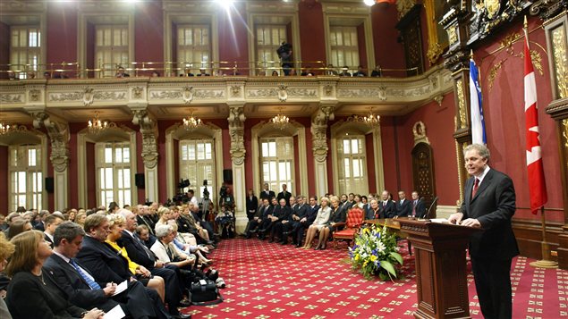 Jean Charest dans la salle du conseil législatif. On peut y voir le drapeau canadien.