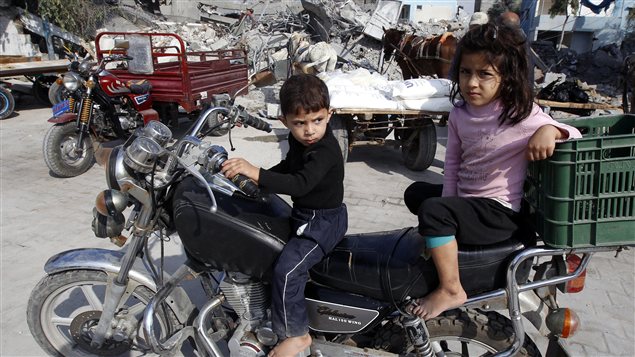 Des enfants palestiniens sur une motocyclette attendent à l’extérieur d’un centre de provision de l’ONU.