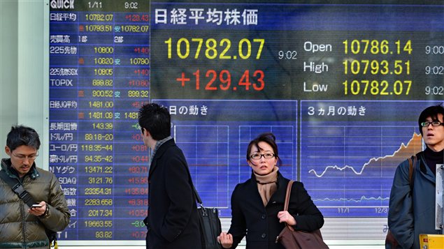 Des Japonais marchent devant un écran montrant les cours de la bourse, alors que le gouvernement vient d'annoncer un plan de relance économique.