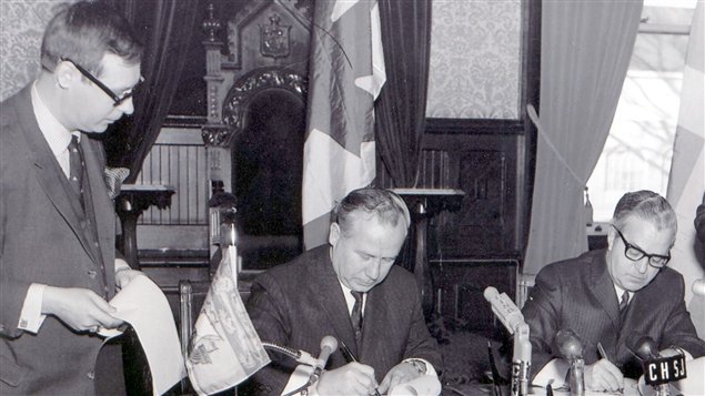 Cette photo fut prise � Fredericton, le 18 d�cembre 1969, lors de la signature du premier accord de coop�ration entre le Nouveau-Brunswick et le Qu�bec. De gauche � droite : M. Robert Pichette, le chef de Cabinet; M. Louis Robichaud, premier ministre du Nouveau-Brunswick; et M. Jean-Jacques Bertrand, premier ministre du Qu�bec.