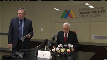 David Arnot, commissaire en chef de la Commission des droits de la personne de la Saskatchewan, est assis devant les micros