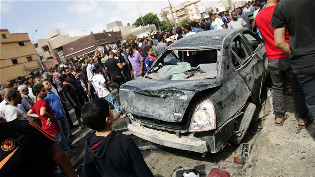 Des curieux se rassemblent autour de la carcasse d'une voiture ayant explosé près d'un hôpital de Benghazi, en Libye.