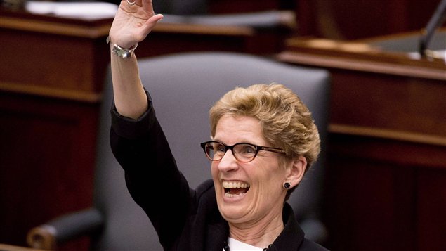 A happy Premier Wynne  raises her right arm in triumph in the Ontario Legislature.