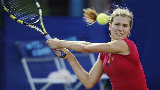 Eugenie Bouchard, wearing a crimson dress, completes a two-handed backhand drive.