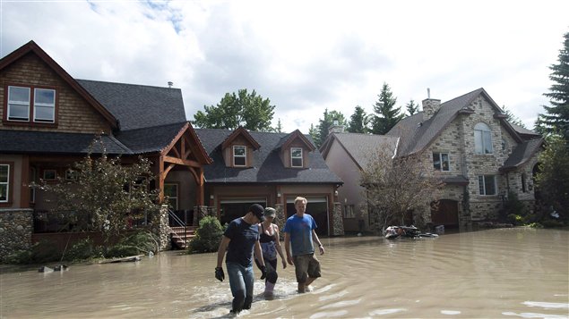 Three people wade trough knee-high flood waters in June. A new survey finds very few Canadians are set financially for emergencies.
