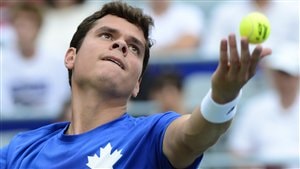 Milos Raonic in blue t-shirt with white maple leaf prepares to unleash a big serve