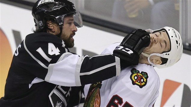 Los Angeles Kings winger Justin Williams on the left in a black jersey with number 14 on the right sleeve fights with Blackhawks centre Andrew Shaw in white jersey number 65 in front of the boards during the Stanley Cup playoffs in June. Williams is administering what is known in hockey as a 