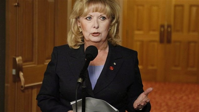 Pamela Wallin at a microphone in a foyer of the Canadian Parliament gestures with her right hand in defending herself earlier this year against charges that she claimed travel expenses she was not entitled to.