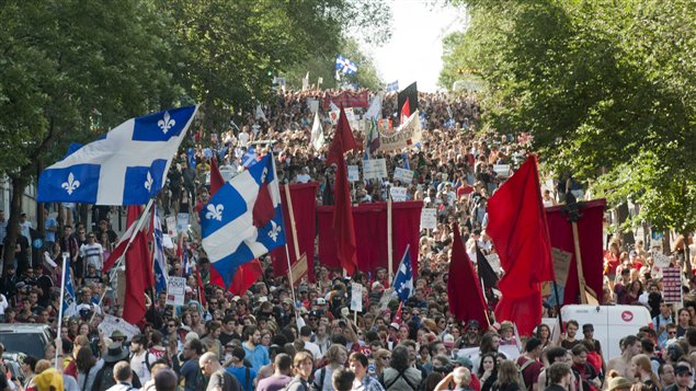 Quebec flags rise above a mass demonstration in Montreal in August of last year. Mixed with the Quebec flags are red banners, symbol of the student movement. The demos prompted a new phrase to be  added to Le Petit Robert dictionary.