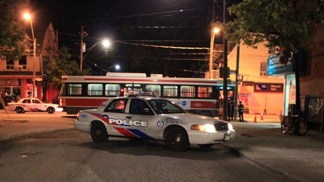 A still from a video posted to YouTube by user Martin Baron shows Toronto police in an altercation with 18-year-old Sammy Yatim on a streetcar in Toronto early Saturday morning, July 28.  Ontario's governing Liberals announced Tuesday that frontline police officers will now be allowed to carry stun guns or Tasers. The photo shows a police car parked to the side of the stopped streetcar. Street lights lit in the background are providing most of the light in the photo, giving it an eerie quality. We see several police in front of the streetcar. Another police car is stationed to the left of the photo, behind the streetcar.