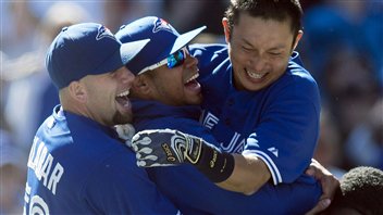 Jays utility infielder Munenori Kawasaki (right) leaps into the arms of pitchers Esmil Rogers (centre) and Steve Delabar (left) after hitting the game-winning walk off double against Baltimore Orioles. Despite a .220 batting average, Kawasaki's constant hustle has made him a fan favourite. Kawasaki in the centre right of photo is grinning widely, as are Rogers and Delabar. All are in their blue jerseys.