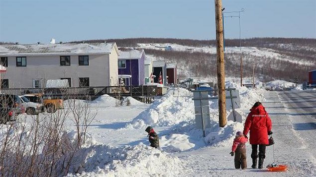 A women in a red parka is walking down a snowy street in Inuvik with her two small children. 