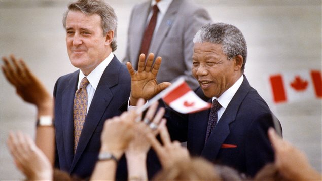 Nelson Mandela (D) salue la foule lors de son arrivée à Ottawa le 17 juin 1990. Il est en compagnie du premier ministre Brian Mulroney (G).