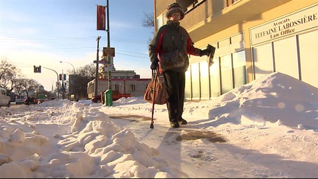 Une aînée se déplaçant à l'aide d'une canne s'aventure sur un trottoir enneigé dans le quartier Saint-Boniface de Winnipeg le 9 décembre 2013.