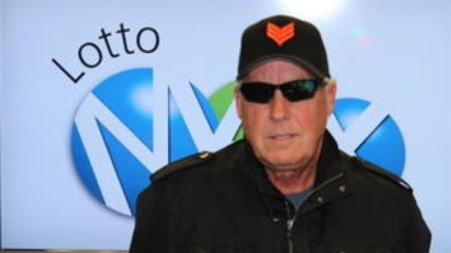 Tom Crist, gagnant du gros lot de 40 millions de dollars au Lotto Max en mai 2013, pose pour sa photo officielle de gagnant avec une casquette et des lunettes fumées.