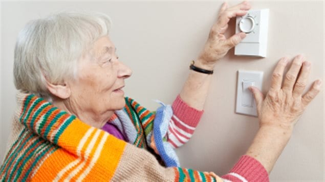 Une dame âgée ajuste le chauffage de sa maison