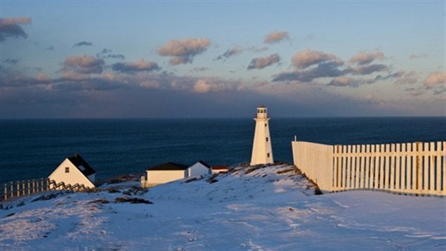 A lighthouse towers over the Atlantic in purple light. A white picket fence is in the foreground.