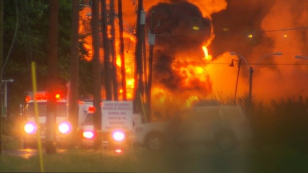 Smoke rises from railway cars that were carrying crude oil after derailing in downtown Lac-Megantic Que., on Saturday, July 6. The photo shows bright flames and large clouds of smoke rising in an eerie yellowish light.