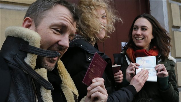 Greenpeace International activists, from left: Philip Ball of the United Kingdom, Sini Saarela of Finland and Alexandra Harris of the United Kingdom show their passports with permission to leave Russia to journalists, near the Federal Migration Service in St. Petersburg, Russia, on Thursday. The trio is all smiles in what appears to be a overcast day with the wind blowing the women's hair. Two Canadians are among those freed.