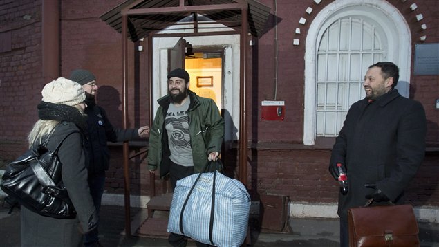 Greenpeace International activist Alexandre Paul leaves a jail after being freed on bail in St. Petersburg inNovember. Paul, the front of his parka unzipped, has a wide smile and is carrying an enormous blue and white duffel bag as he is greeted by three well-wishers outside the half-open door of the grey-walled prison on what appears to be a dark and gloomy night.