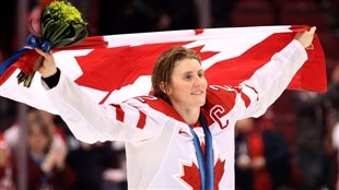 Team Canada captain Haley Wickenheiser holds flowers in her right hand and the Canadian flag in both hands above her head as she celebrates Team Canada's third consecutive Olympic gold, at the Vancouver 2010 Games.
