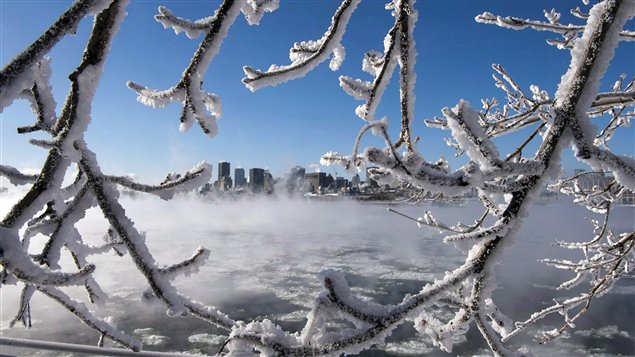 Ice fog from the St. Lawrence river blankets the city as windchill temperatures hit -38C Wednesday in Montreal. People are still without electricity in Eastern Canada as a result of the winter storm that hit 11 days ago. The photo has trees covered in ice and snow in the foreground. Across the river, we see the city of Montreal.