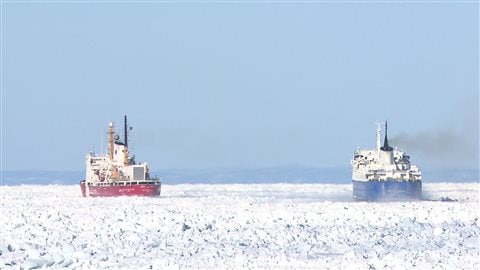 Un brise-glace de la Garde-Côtière aide un naviere marchant à se tracer un chemin dans les glaces du Fleuve Saint-Laurent.