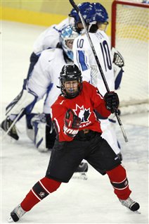 Katie Weatherston wheels away from the net in celebration in her red Team Canada sweater after her goal against Team Finland during first period ladies hockey semi-final at the Turin 2006 Winter Olympic Games. Her stick in her left hand is raised, her right hand is clenched in a fist pump.