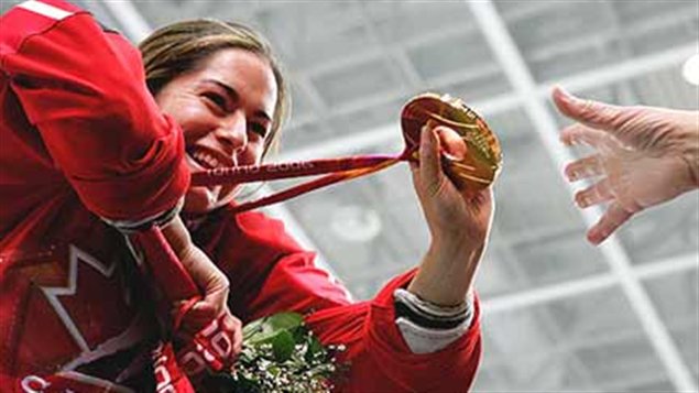Katie Weatherson is all smiles in her Team Canada red jersey as she holds an Olympic Gold medal in her left hand and a bouquet of flowers in her left hand at the 2006 Turin Olympics