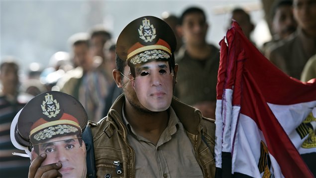 بائع متجول في الجيزة جنوب القاهرة يحمل أعلاماً مصرية وأقنعة على صورة وزير الدفاع الفريق أول عبد الفتاح السيسي أمس بجوار مركز اقتراع ينتظر أمامه الناخبون دورهم في اليوم الثاني والأخير للاستفتاء على مشروع الدستور المعدل