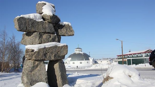 A picture of an Inuit inukshuk in the foreground in downtown Inuvik located in Canada's Northwest Territories. An igloo church is in the background.