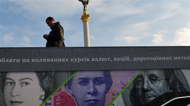Un hombre pasa cerca de un afiche publicitario que muestra billetes de banco británicos, ucranianos y estadounidenses, cerca de la plaza de la independencia, en Kiev (archivo)