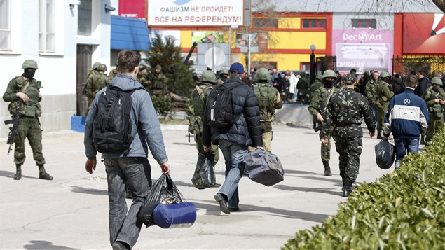 Soldados ucranianos vestidos de civil salen de la base de Sebastopol, bajo la mirada de los milicianos pro rusos.